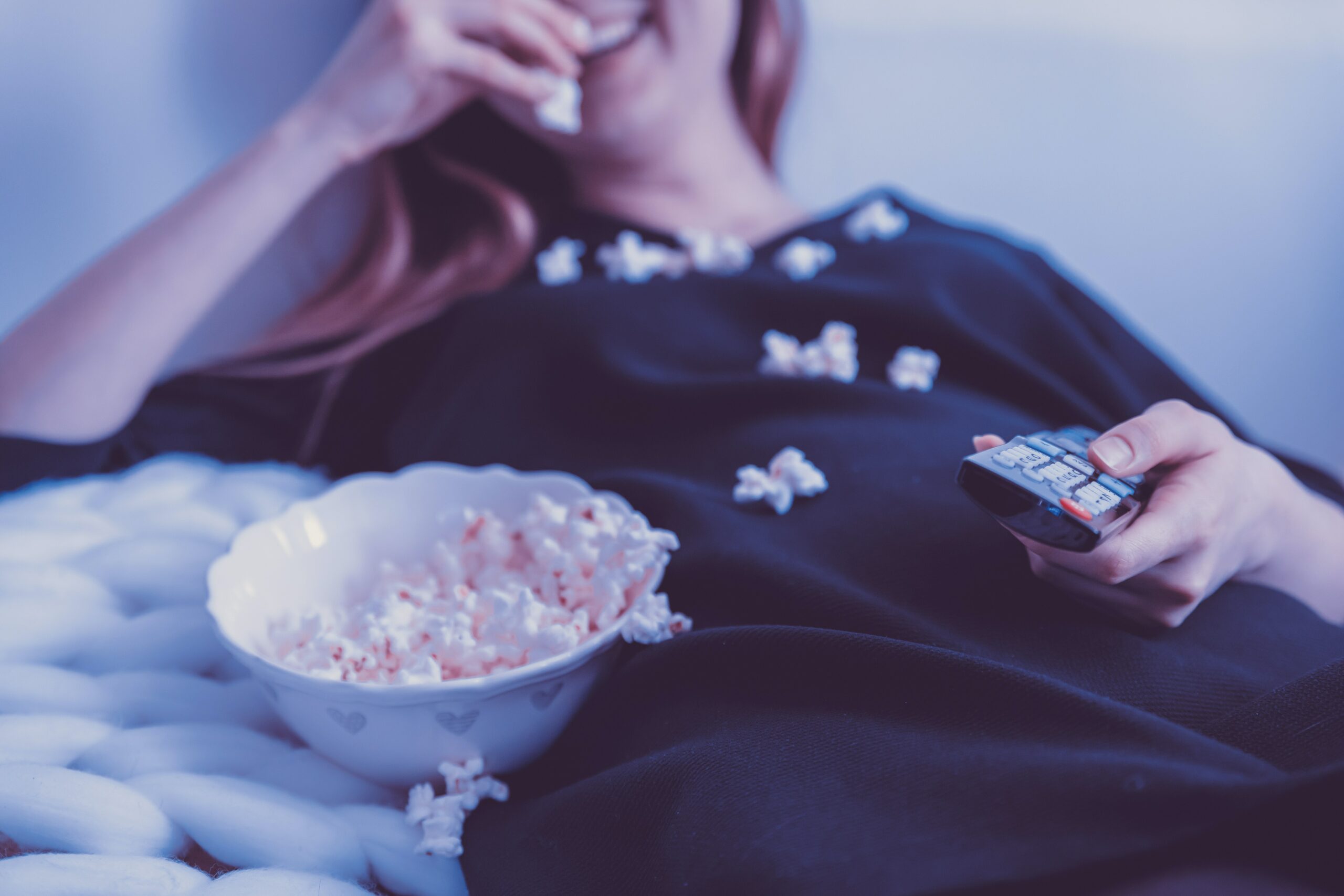 Femme allongée en train de manger de pop-corn en regardant plusieurs séries