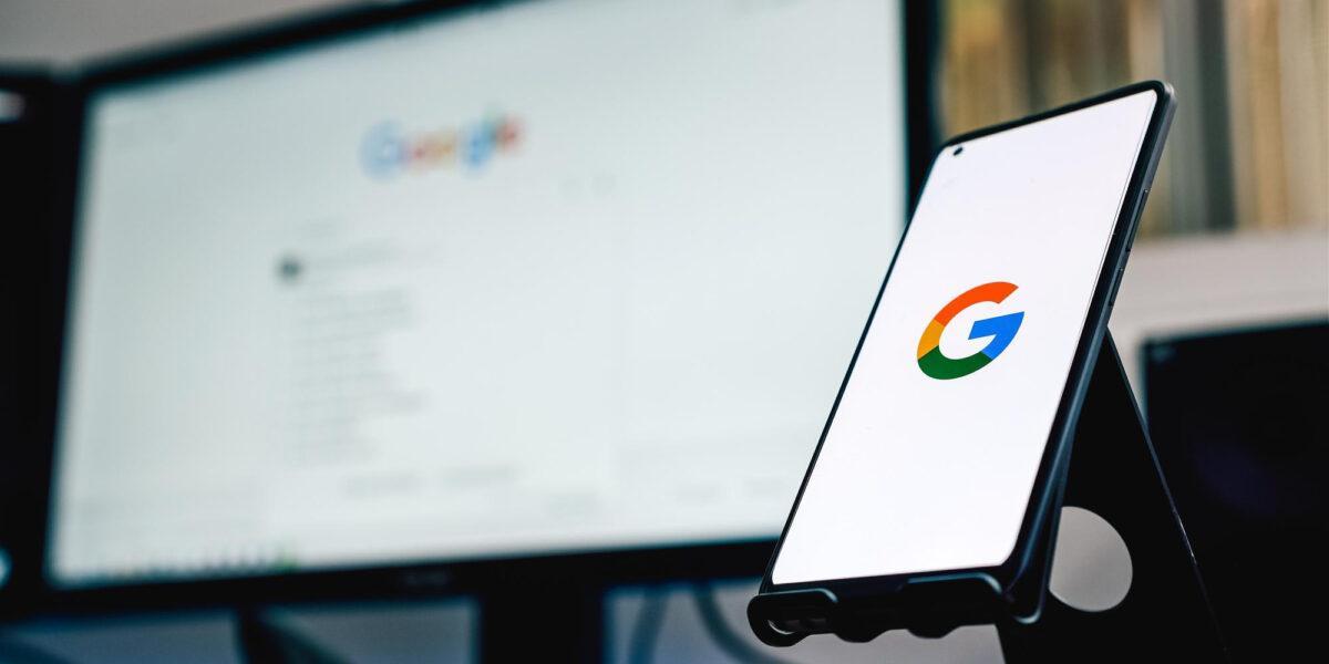 Photo d'un téléphone avec le logo google en premier plan et d'un ordinateur étant également sur google en second plan flouté