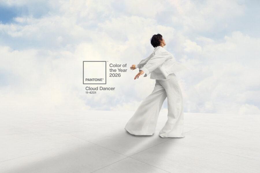 Une personne habillée tout en blanc danse avec les bras ouverts devant un ciel nuageux, accompagnée du logo Pantone "Color of the Year 2026 - Cloud Dancer 11-4201".
