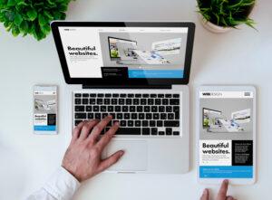 Image montrant un ordinateur portable, une tablette et un téléphone avec un site webdesign affiché et une main sur le clavier 