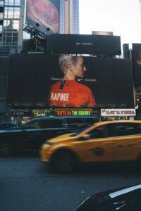 Grand panneau publicitaire Nike à Times Square affichant l'athlète Megan Rapinoe avec le slogan "Dream with us", surplombant une rue animée de New York avec un taxi jaune en mouvement.