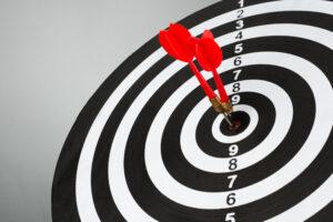 Gros plan d'une cible de fléchettes noire et blanche avec deux fléchettes rouges plantées exactement dans le mille (bullseye), symbolisant la précision du micro-ciblage publicitaire.