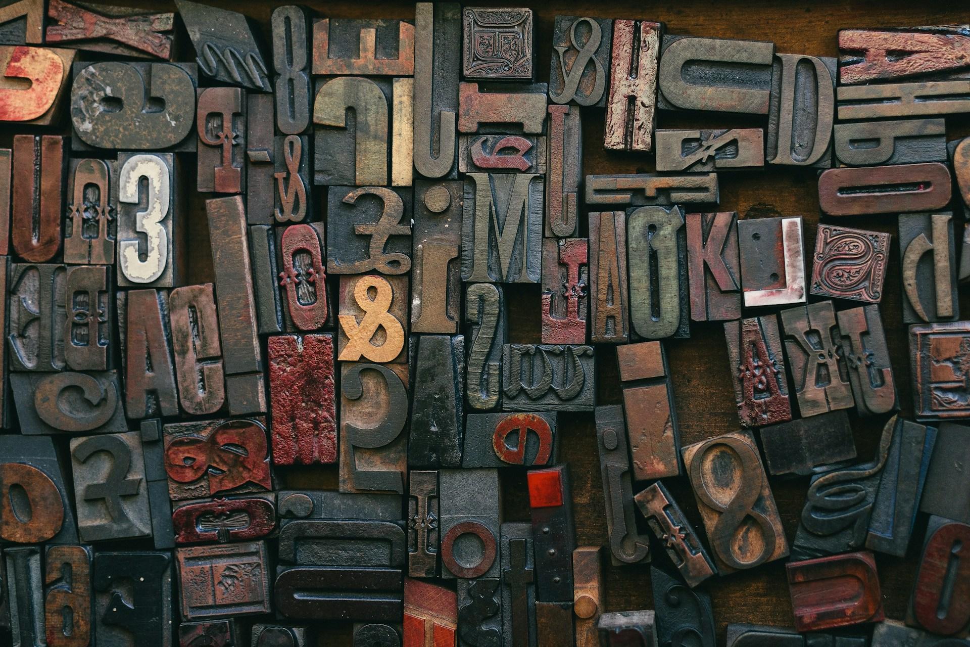 Collection de caractères typographiques anciens en bois et en métal, disposés en mosaïque sur un fond sombre.