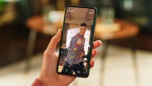 Main tenant un smartphone affichant une vidéo verticale de type TikTok ou Instagram Reel, montrant un créateur de contenu souriant dans une interface de réseau social interactive.